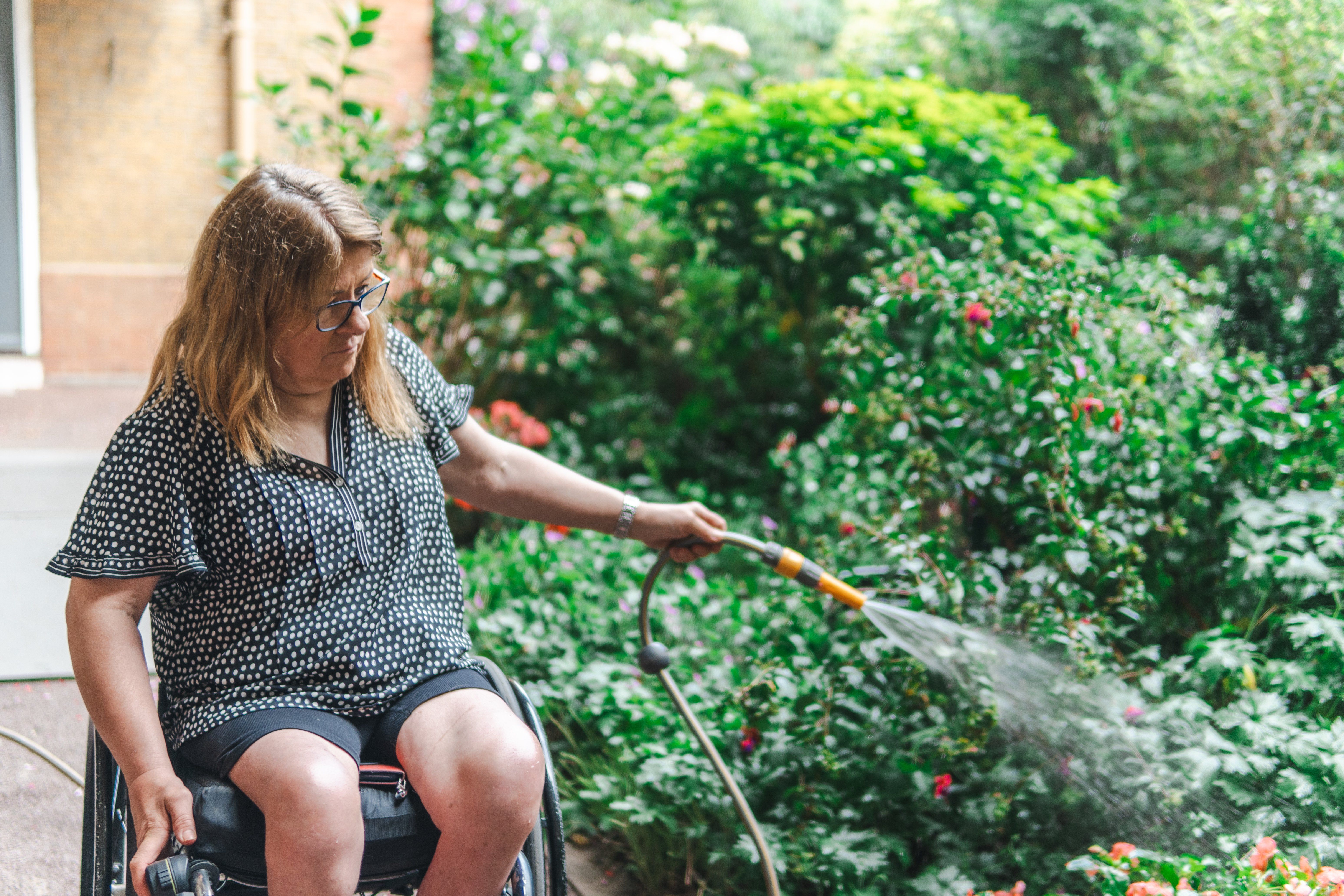 A woman using a wheelchair watering plants in a garden